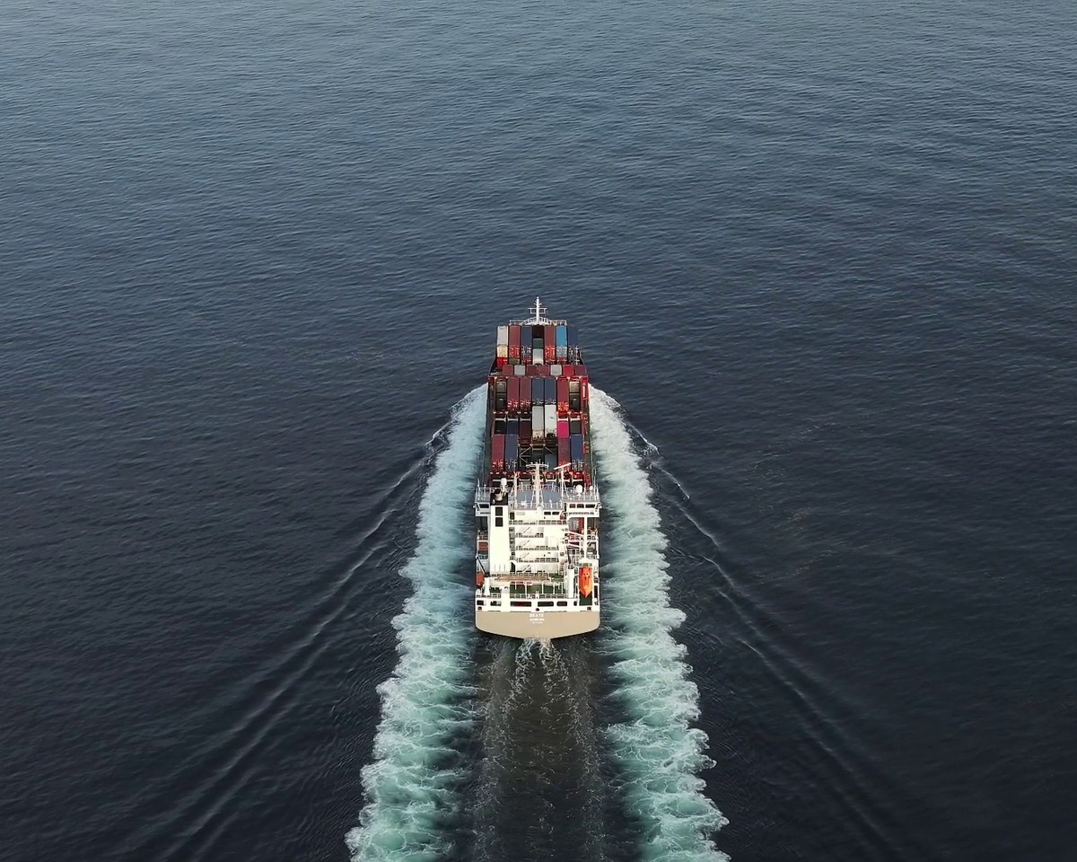 A commercial cargo vessel underway at sea, leaving a broad wake